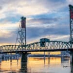 Steel bridge over a calm river at sunset.