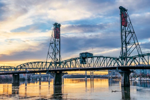 Steel bridge over a calm river at sunset.